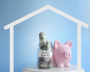 This is an image of a piggy bank and a glass jar of money next to it. The jar has the words home equity on it. There is a white outline of a house around the piggy bank and jar.